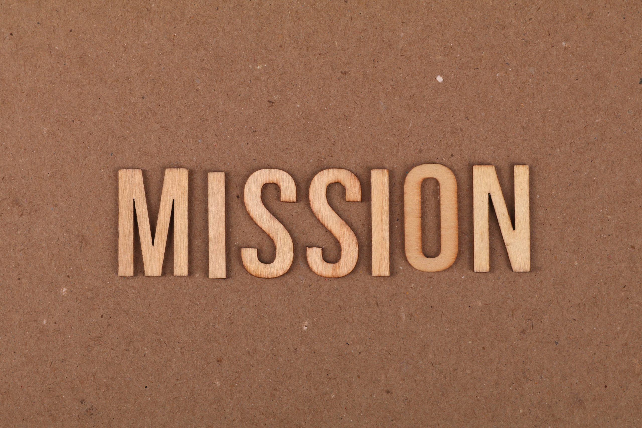 Wooden letters spelling 'MISSION' on textured cardboard background, emphasizing goals and purpose.
